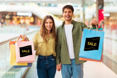 Modern AVM 'de indirimli satış teklifi sunan, kameraya gülümseyen mutlu çift alışveriş torbaları. Alışveriş, Kara Cuma Konsepti. Kolaj