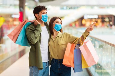 Şuraya bak. Alıcı çift alışveriş yapıyor ve alışveriş merkezlerinde koruyucu maske takan alışveriş torbalarıyla yan yana poz veriyorlar. Kara Cuma Satış Sezonu