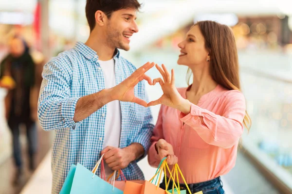 Kupujący Para Zakupy Making Fingers Heart Pozowanie Trzymając Torby Shopper — Zdjęcie stockowe