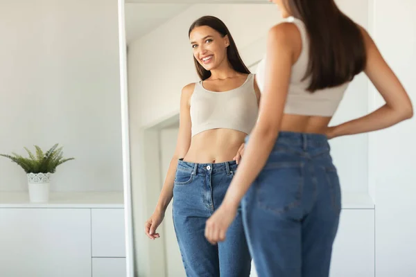 体重減少後の鏡の中で彼女の反射を見て笑顔をポーズ魅力的な女性は自宅に立って 自信作 選択的フォーカス クロップ — ストック写真