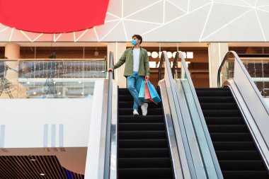 Kara Cuma. Yüzü maskeli, alışveriş torbası taşıyan bir adam hafta sonu Hypermarket 'te taşınan merdivenlerde duruyor. Satış sezonu teklifi. Tam Uzunluk