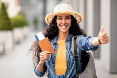Seyahat, tatil, turizm. Pasaportu uçuş biletleriyle gezen, kameraya gülümseyen, sırt çantası taşıyan, fotokopi çeken çekici bir orta doğulu kadın.