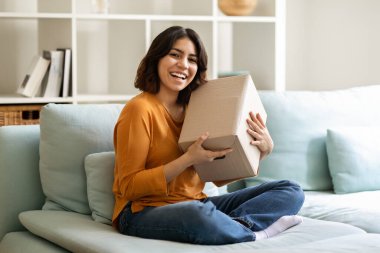 Teslimat Konsepti. Memleketinde büyük bir teslimat kutusuyla mutlu Arap kadın pozu, koltukta oturan ve paketleri elinde tutan neşeli Orta Doğulu kadın, hızlı nakliyatın keyfini çıkarıyor, kopyalama alanı.