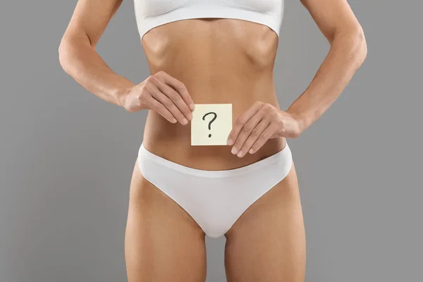 Womens Health. Young Female In White Underwear Holding Card With Question Mark Near Her Belly, Closeup Shot Of Unrecognizable Slim Lady In Panties Posing Over Grey Studio Background, Copy Space