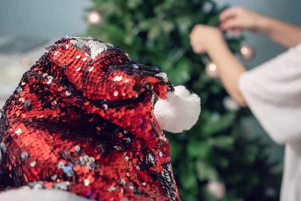 Kadın elleri Noel ağacını toplar ve oyuncaklarla süslüyor. Kırmızı Noel Baba Şapkası Noel ağacında. Yeni yıl havası. Parti ve tatil kutlaması konsepti