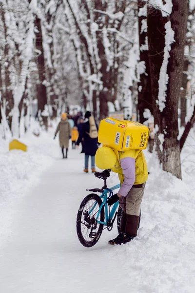 Краснодар, Россия - 24 января 2022 года: Курьер, курьер с тепловой сумкой на спине, чинит велосипед — стоковое фото