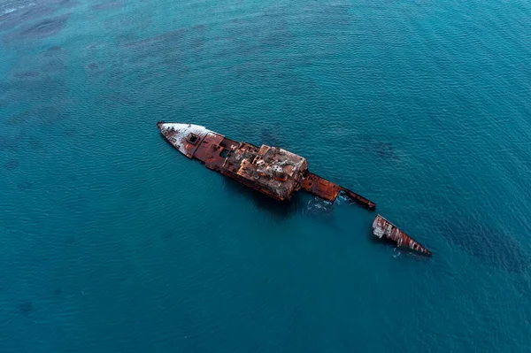 A sunken shipwreck on the reef, a dry cargo ship lies on the bottom of the port side, slowly rusts and collapses. A large seagoing dry-cargo vessel washed ashore in a strong gale, breaking it in two, covered in red rust.