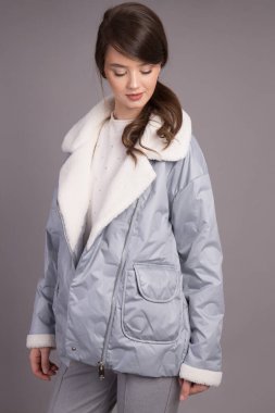 Stüdyoda gri arka planda giysileri gösteren bir model çekmek. Genç bir kız model kameraya poz veriyor. Kıyafetleri farklı pozisyonlarda gösteriyor..