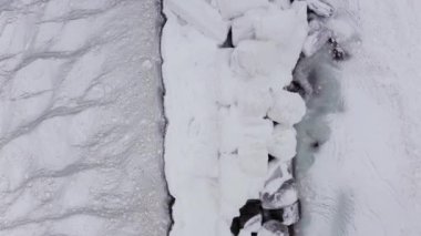 Kuzeyde soğuk bir kış günü, buzun içinde donmuş bir deniz feneri var. Buz limanı beyaz buzla kaplı, yukarıdan gelen hava manzaralı..