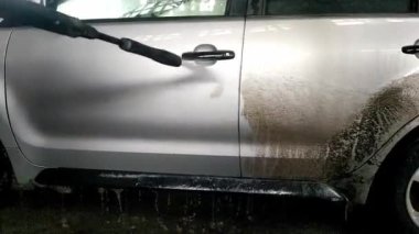 Araba yıkama makinesi kirli bir arabayı yüksek basınçlı suyla yıkıyor. Kirli bir araba, yüksek basınçlı bir jetle bir oto yıkama makinesi tarafından temizlenir..