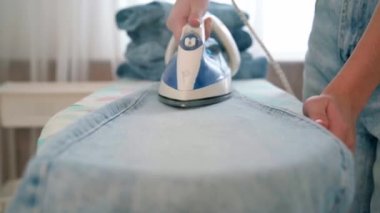 Bir kadının eli buhar etrafında kızgın bir ütü tutar. Hizmetçi kıyafetlerle çalışır, onları ütüler ve sepete koyar. Genç bir kız ütü masasında temiz giysiler ütülüyor..