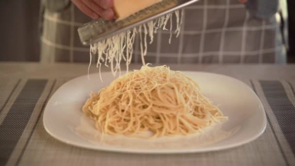 El cocinero en la cocina frota el queso duro en un plato de pasta con pasta italiana recién preparada frota el queso. Con pasta italiana recién preparada, el chef frota queso duro en un rallador de hierro en un — Vídeo de stock