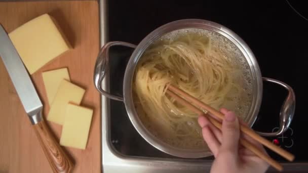 Ze świeżo przygotowanym włoskim makaronem kucharz wrzuca makaron na patelnię i miesza pałeczkami. Szef kuchni gotuje makaron, aby przygotować pyszne danie. — Wideo stockowe