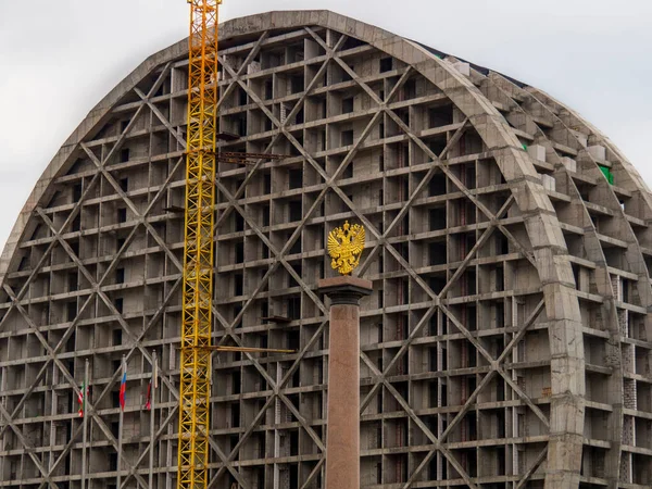 The golden coat of arms of the Russian Federation on the background of a building under construction.