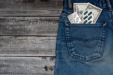 Kot pantolonun arka cebinde bir paket hap. Ahşap bir masanın arka planında pantolon cebinde dolar banknotları. Mevsimsel grip virüsü konsepti.