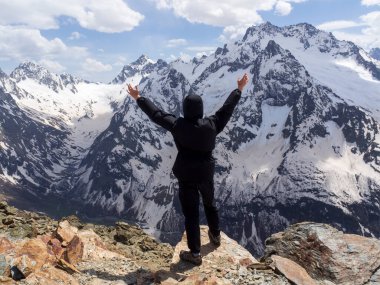 Siyah turist elbiseli bir adam karlı bir kayanın arkasında poz veriyor. Kafkas Dağları, Dombay.