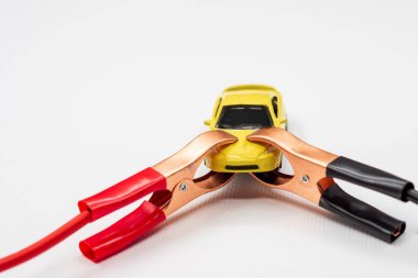 Kırmızı ve siyah kablo otomotiv klipleri ya da beyaz arka planda sarı oyuncak bir arabanın akü kıskaçları. Kışın otomobil motorunu çalıştırmak, pilin hızlı bir şekilde başlatılması konsepti.