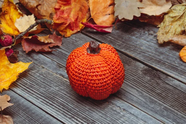 一个橙色的玩具南瓜放在灰色的乡村木桌上 背景是秋天干枯的树叶 万圣节和感恩节装饰的概念 — 图库照片