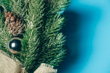 Süslemeleri ve konileri olan küçük plastik bir Noel ağacı mavi bir arka planda yatıyor. Yapay ladin dalları yakın plan. Kopyalama alanı metin eklemek için bir yerdir.