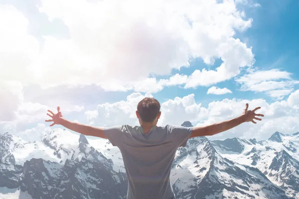 Gri tişörtlü bir adam kar kaplı kayaların arkasında poz veriyor. Kafkasya Dağları, Dombai 'yi kucaklayan bir erkeğin arkadan görünüşü.