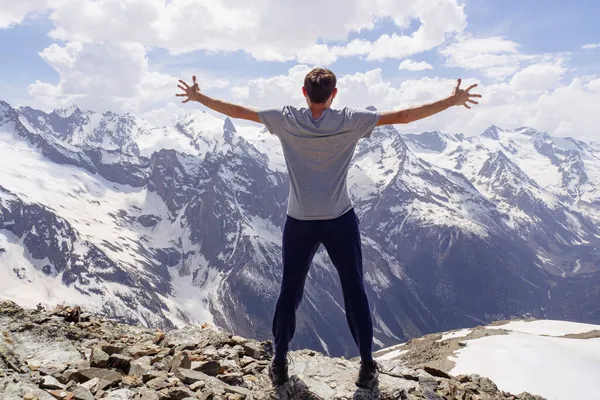 Gri tişörtlü bir adam kar kaplı kayaların arkasında poz veriyor. Kafkasya Dağları, Dombai 'yi kucaklayan bir erkeğin arkadan görünüşü.