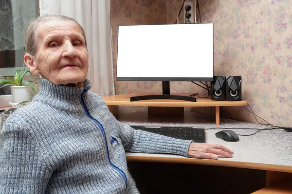 A modern grandmother of 70 years is sitting at the computer. An elderly woman proudly smiles against the background of a white PC screen. The concept of Internet communication, winning the game.