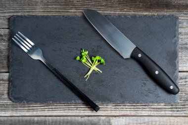 Siyah tahta üzerinde mikroyeşil bir tahta üzerinde servis çatalı ve tahta bir masa arkasında bıçak. Sağlıklı beslenme, vejetaryen yemek kavramı..