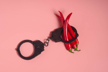 Pembe arka planda siyah polis kelepçeleri içinde bir sürü kırmızı kırmızı kırmızı kırmızı biber yatar. Cinsel suçlar kavramı. Şiddet ve tacizin cezası.