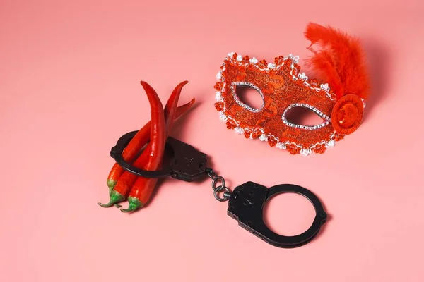 Pembe arka planda geleneksel Venedik karnaval kırmızı maskesi. Polis kelepçeli kırmızı acı biber. Düz yerde, üst tarafta. Seks ve fuhuş kavramları.