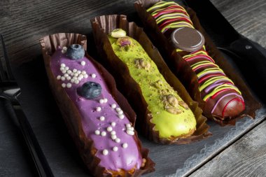 Çerez, çikolata ve yaban mersinli renkli camlarla kaplı üç farklı eklem servis çatalı ve bıçaklı bir tahta üzerinde. Yüksek kalorili gıda kavramı.