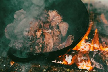 Cooking meat in a cast iron boiler on a campfire close up. Beef and mutton are fried on fire. Oriental traditional Asian cuisine. Travel dinner in the forest.