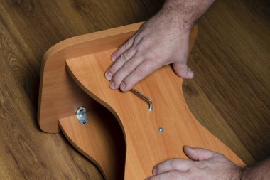 Bir erkek elinde büyü anahtarı olan bir tabureyi toplar ya da tamir eder..