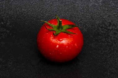 Yeşil yapraklı kırmızı domates ve siyah arkaplanda su damlaları..