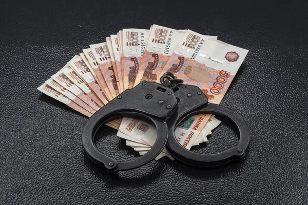 Birçok beş bin Rus para banknotu, siyah polis kelepçeli ahşap bir arka planda bir pervanenin içinde yatıyor. Ekonomik suç, hırsızlık veya soygun kavramı.