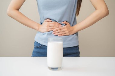Laktoz intolerans konsepti. Kadın elinde bir bardak süt tutuyor ve midesi ağrıyor..
