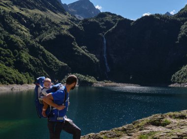 Bebek taşıyıcısının babası dağlarda yürüyüş yapıyor. Aile macerası, açık hava tatili.