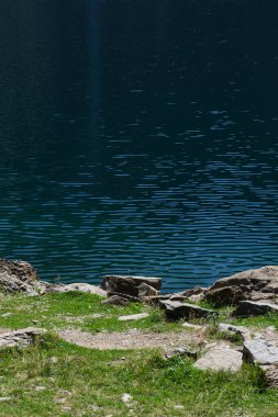 Önünde taşlar ve çimenler olan doğal bir göl suyunun ayrıntıları. Sakin ve ruhaniliğin görüntüsü