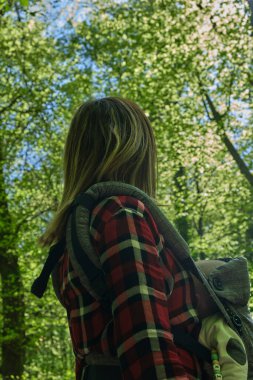 Anne ormanda bebek taşıyıcı çantayla yürüyor. Doğaya seyahat eden aile, küçük çocuklu kadın..
