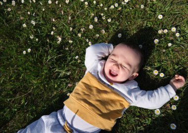 Mutlu ve gülümseyen küçük çocuk çayırda uzanan baharın tadını çıkarıyor..