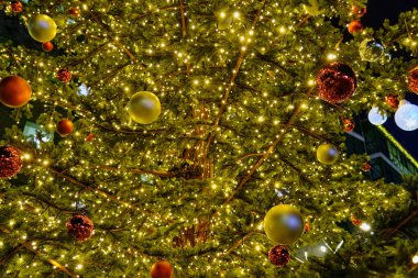 Noel ağacında asılı kırmızı ve altın Noel süsleri ışıklarla aydınlatılmış.