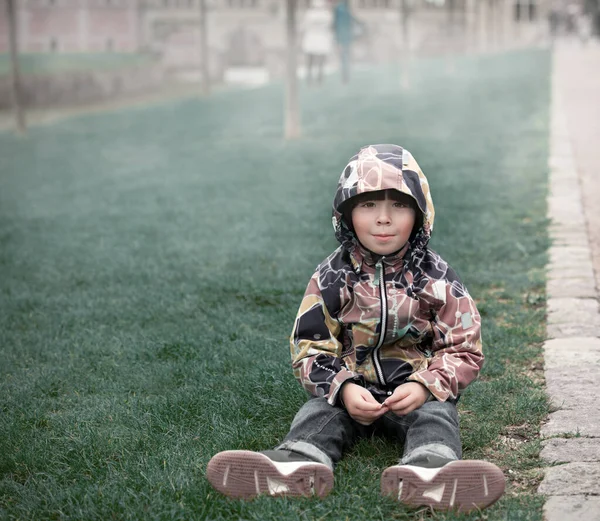 Kleine Jongen Bruine Jas Zit Gras Het Park Mist Achtergrond — Stockfoto