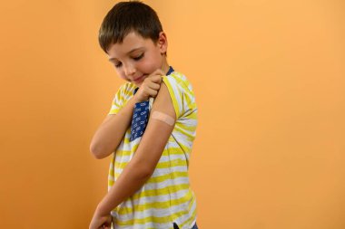 Bir çocuk kolundaki yara bandına bakar. Aşı kavramı