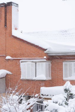 Beyaz kepenkleri ve bacası olan karlı bir ev.