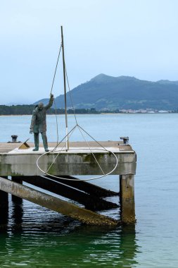 Santona, Cantabria, İspanya. 6 Temmuz 2021: Atlas balıkçısını temsil eden bronz heykel, küçük gümüş bir balık.