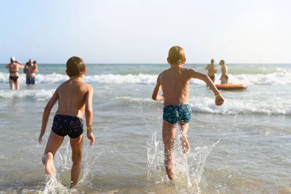 İki çocuk sırt üstü deniz suyuna koşuyor.