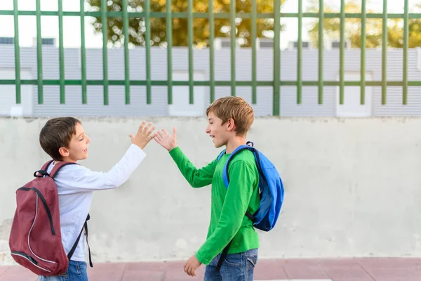 Sırt çantalı iki çocuk birbirlerini beşlikle selamlıyor. Okul konseptine dönelim.