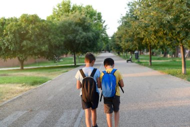 Sırt çantalı iki çocuk parkta geziniyor. Okula dönüş kavramı