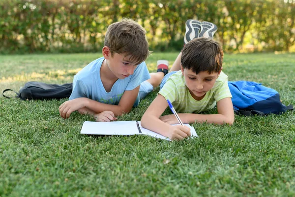 Two Students Lying Park Backpacks One Them Writing Notebook Back — Foto de Stock