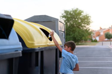 Çocuk geri dönüşüm için sarı kabın içine plastik bir şişe atıyor..