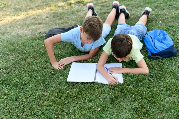 Two Children Lying Grass Park Doing School Homework Notebook — Foto de Stock